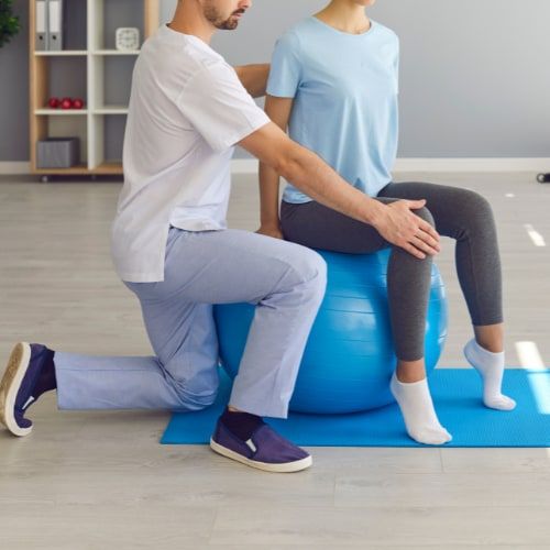 Physiothérapeute guidant le genou d’une patiente assise sur un ballon de rééducation